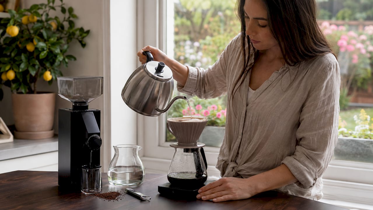 Woman pouring water over coffee in home kitchen