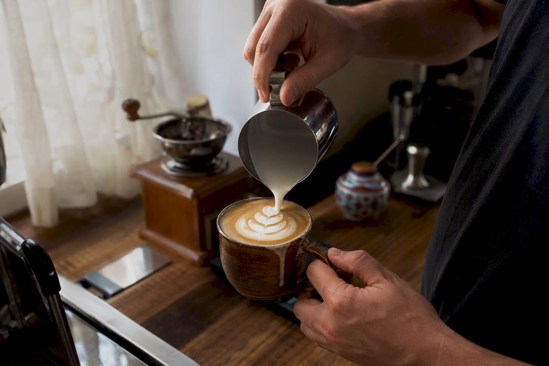Hand pouring heart latte art in home kitchen
