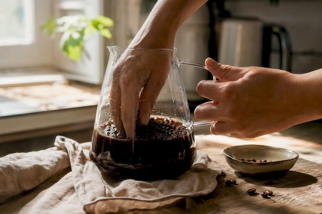 Hands pouring water over cold brew coffee grounds