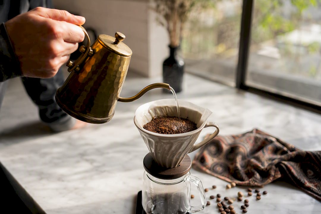 Hand pouring water over coffee grounds in pour-over dripper