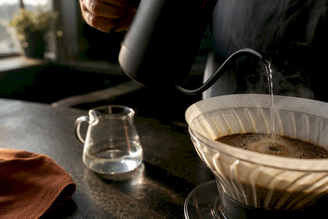 Hand pouring water over coffee grounds